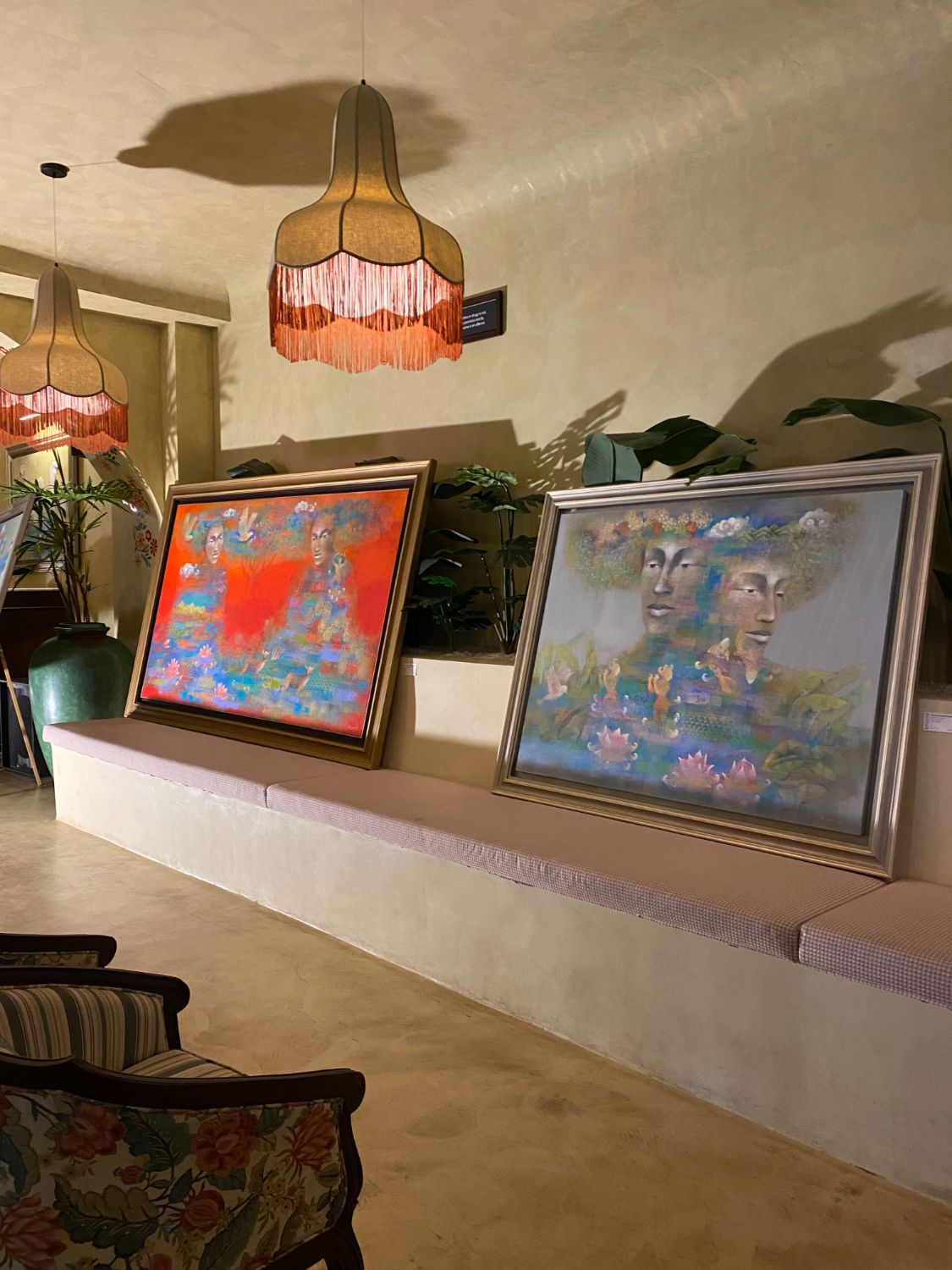 Paintings on a banquette under fringed lamps