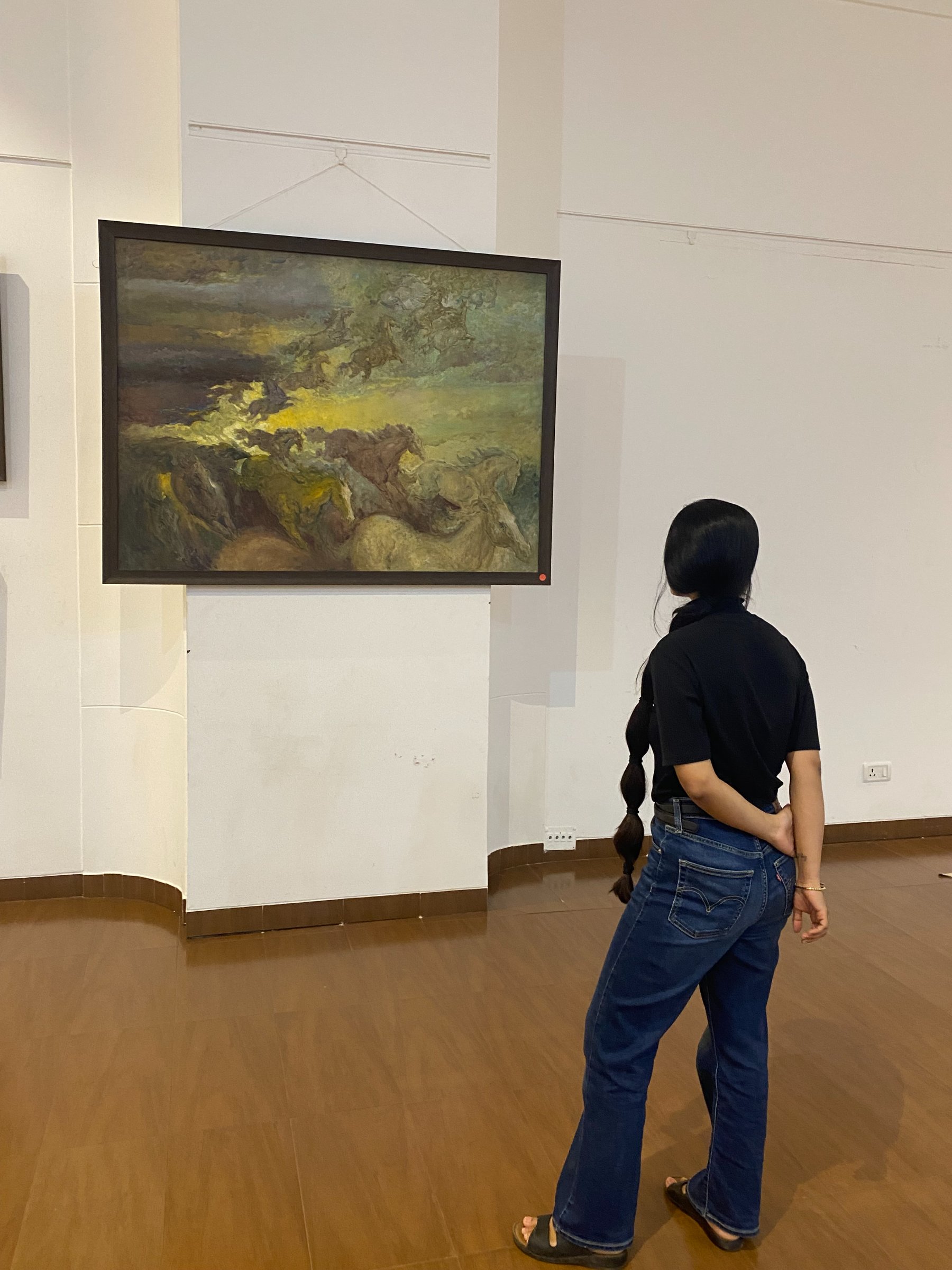 A visitor stands before Horses Fantasy, Late Shri Pratap Mulick’s large oil of horses surging through a storm-lit sky