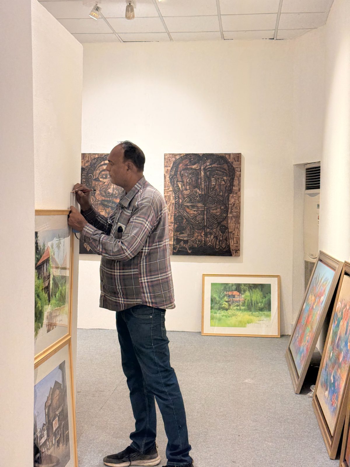 An installer pencilling a mark on the wall beside framed watercolours